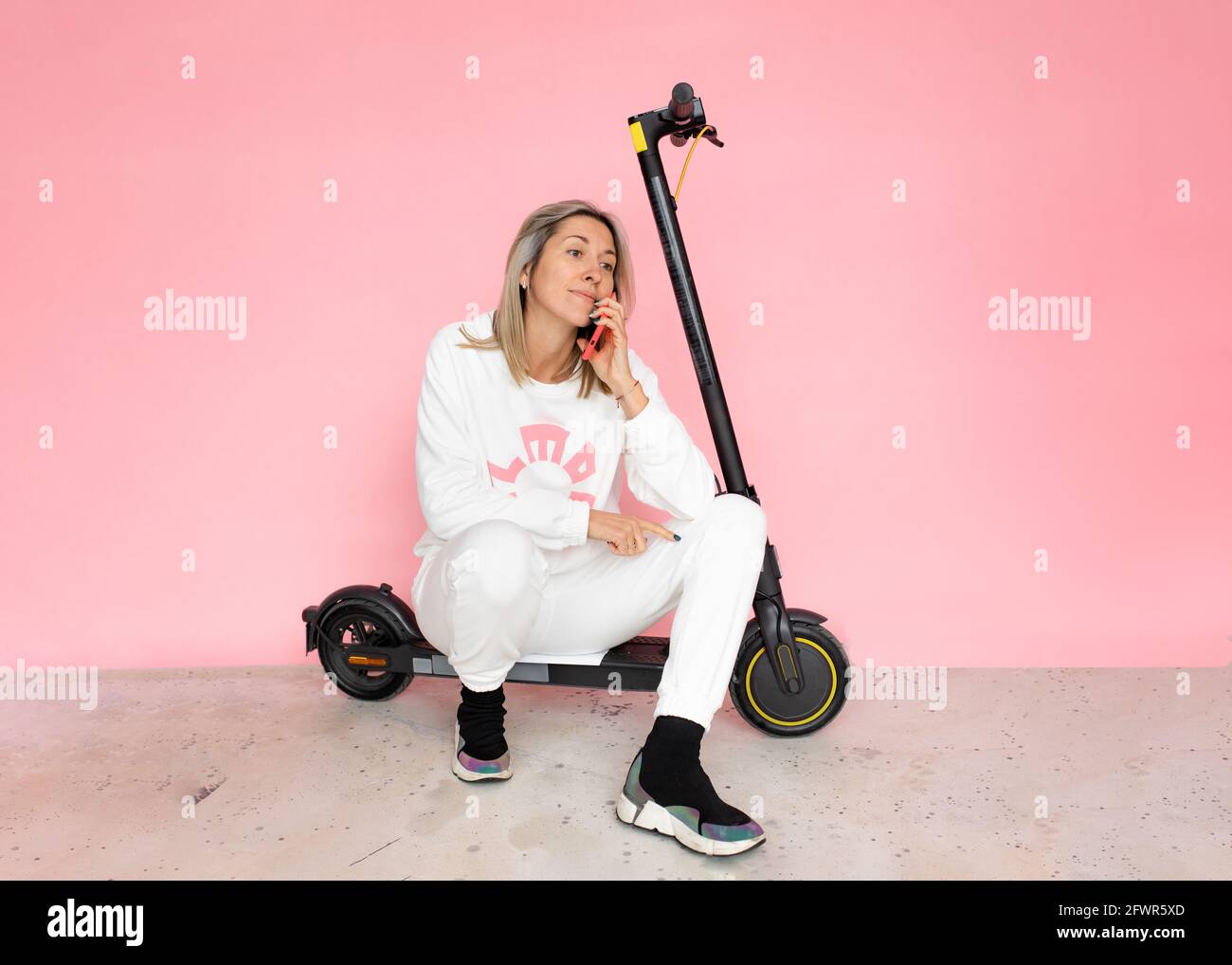 Une femme blonde sur fond rose s'assoit sur un scooter électrique et repose, espace de copie Banque D'Images