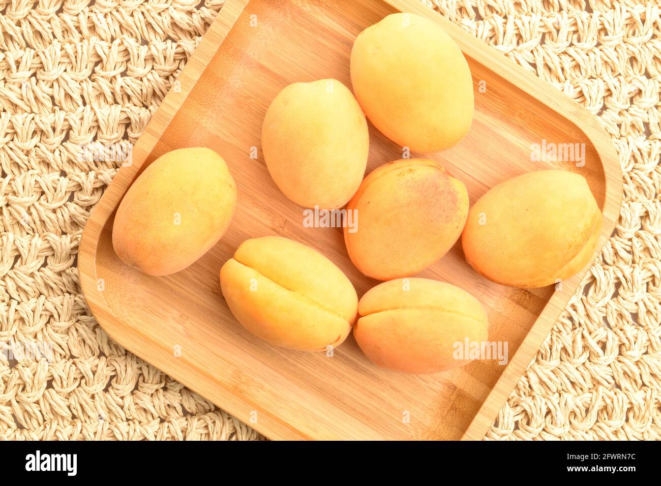 Trois abricots jaune juteux d'ananas sur une assiette de bambou, gros plan, sur un tapis de paille, vue de dessus. Banque D'Images