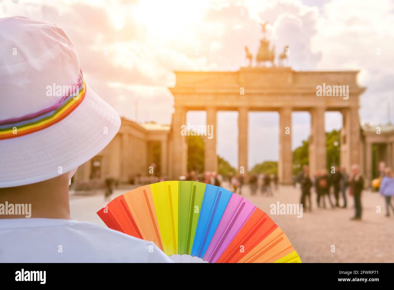 Femme LGBT caucasienne mature à Berlin avec un éventail arc-en-ciel et un ruban sur un chapeau blanc d'été. Arc-en-ciel, symbole de la fierté gay LGBTQIA, diversité. Femme portant Banque D'Images