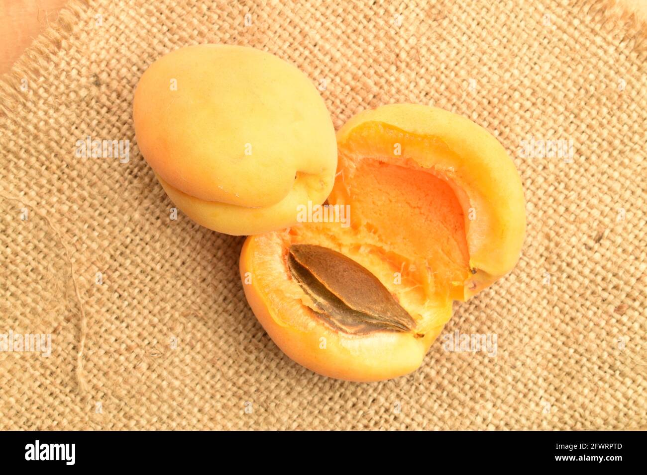 Un abricot entier et un ananas coupé en deux, macro, sur le tissu jute, vue du dessus. Banque D'Images