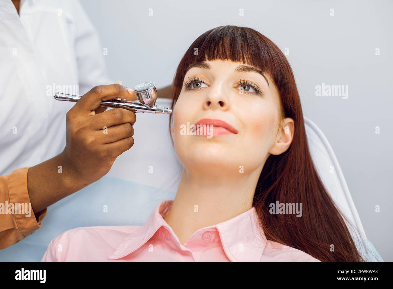 Gros plan du visage de la belle jeune femme caucasienne recevant peeling d'oxygène de visage au centre de cosmétologie. Jeune fille aux cheveux rouges qui apprécie le rajeunissement et la revitalisation de la peau. Biorevitalisation sans aiguille Banque D'Images
