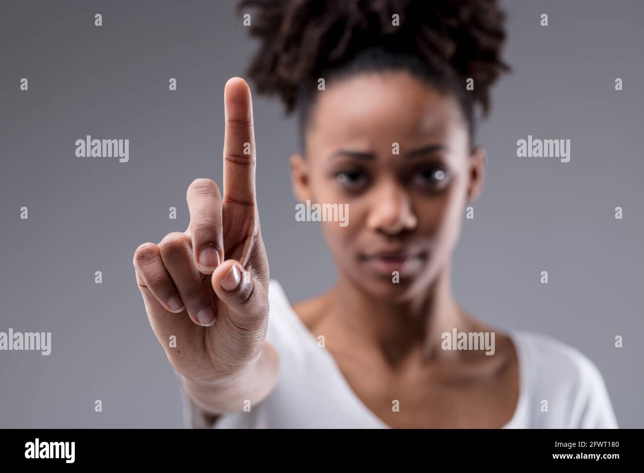 Stern a concentré sa jeune femme en tenant son index comme si elle mettait l'accent sur un point, en appelant à un arrêt ou en s'identifiant sur un backgroun gris studio Banque D'Images