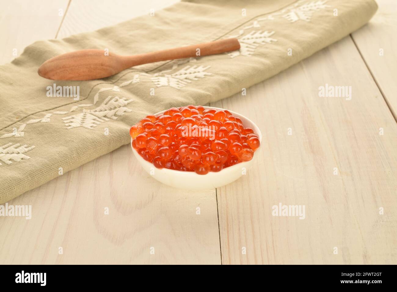 Caviar rouge biologique naturel dans un plat en céramique avec une serviette en lin et une cuillère en bois, gros plan, sur une table en bois blanc. Banque D'Images