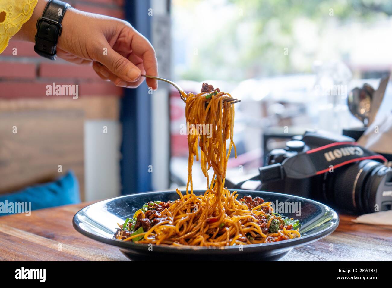 Femme à fourche prenant la rue indo chinese manchurian hakka nouilles alimentaires d'un bol noir placé sur un bois table dans un petit restaurant de rue Banque D'Images