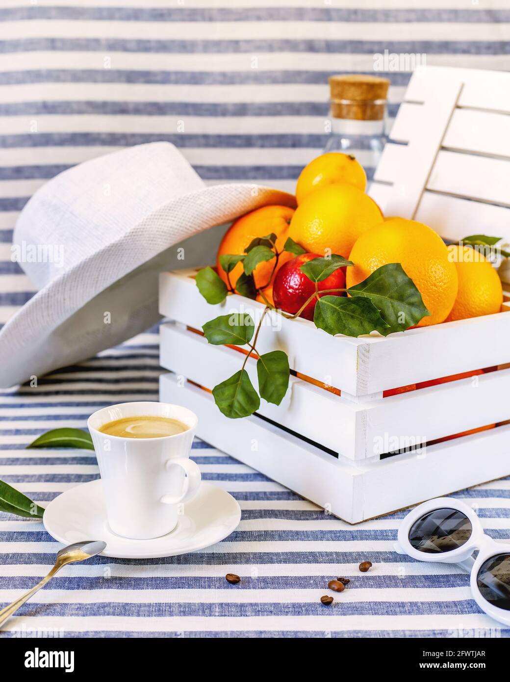 Composition estivale avec une tasse de café, agrumes sur une boîte en bois et accessoires d'été sur un fond textile rayé. Matin méditerranéen Banque D'Images