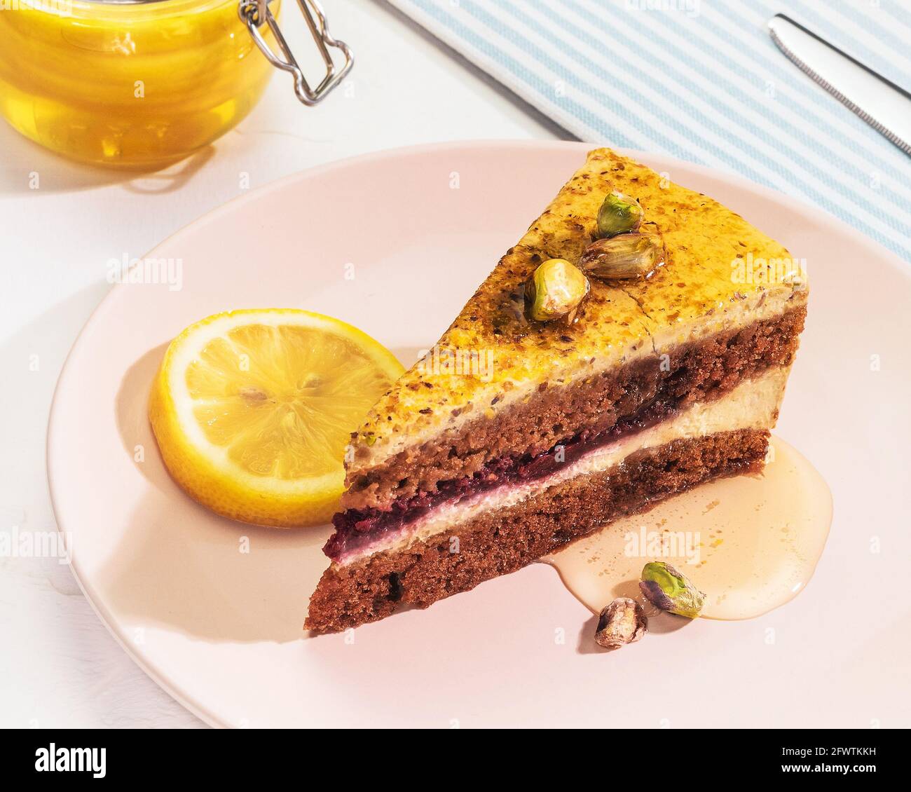 Composition de la nourriture du matin horizontale avec un morceau de tarte au citron pistache avec miel et noix sur une assiette rose avec un pot de miel sur fond blanc Banque D'Images