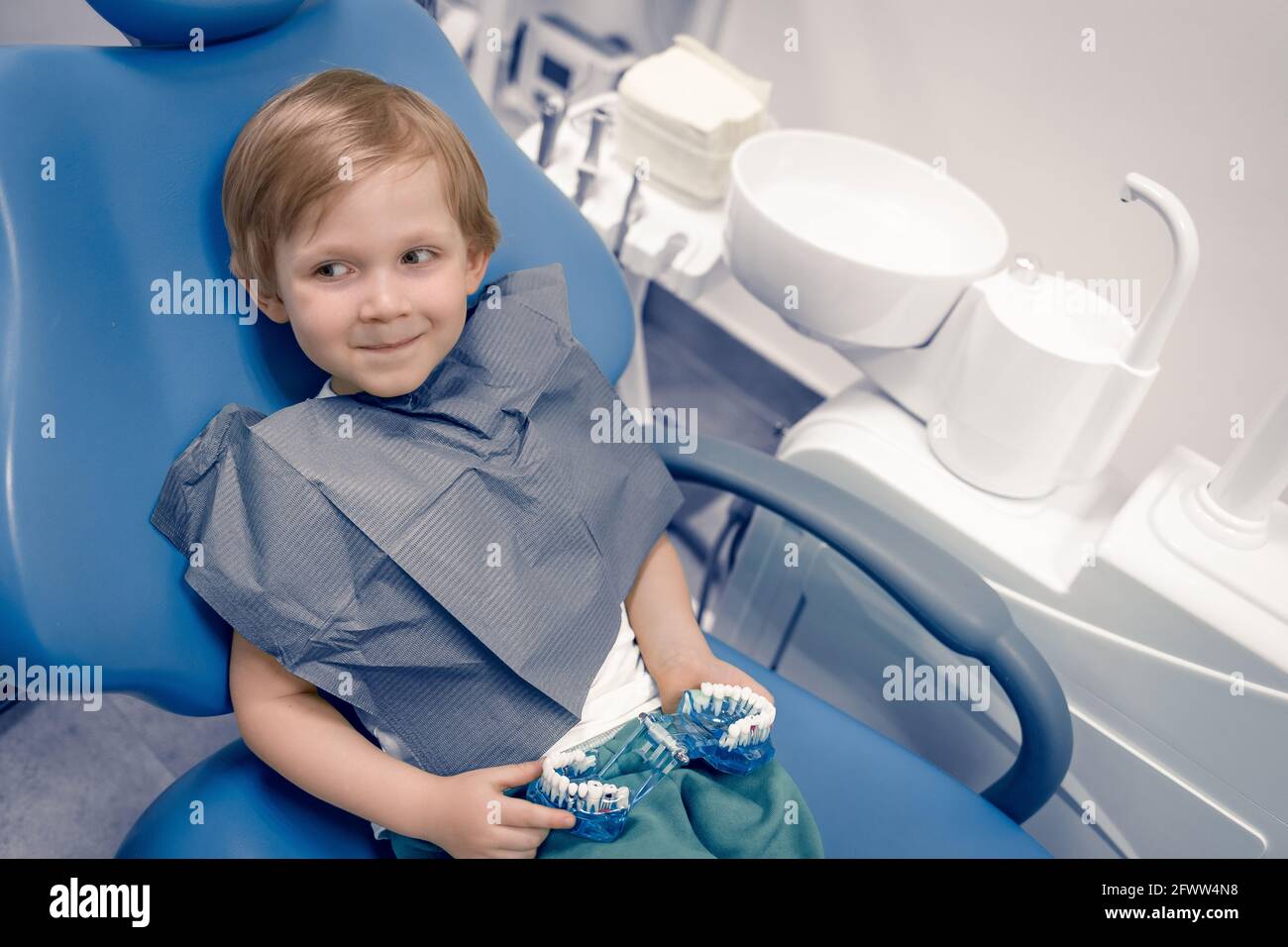 Un enfant de race blanche heureux s'assoit dans une chaise dentaire chez le médecin du dentiste. Préchooler traitant les dents, heureux. Concept publicitaire avec espace de copie. Banque D'Images