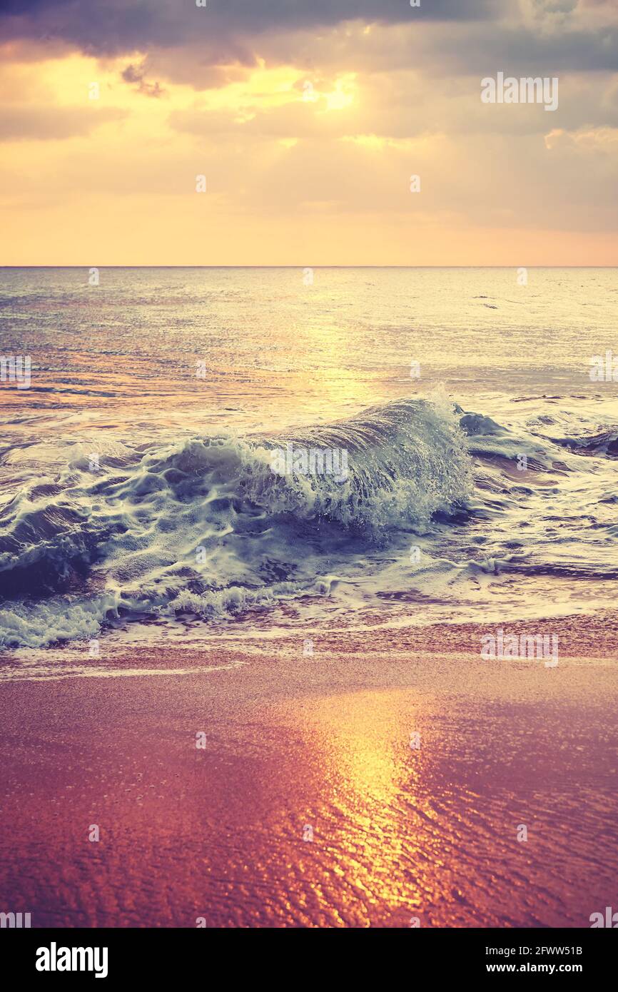 Vue panoramique de surf écrasant sur une belle plage de sable au coucher du soleil, couleurs appliquées. Banque D'Images