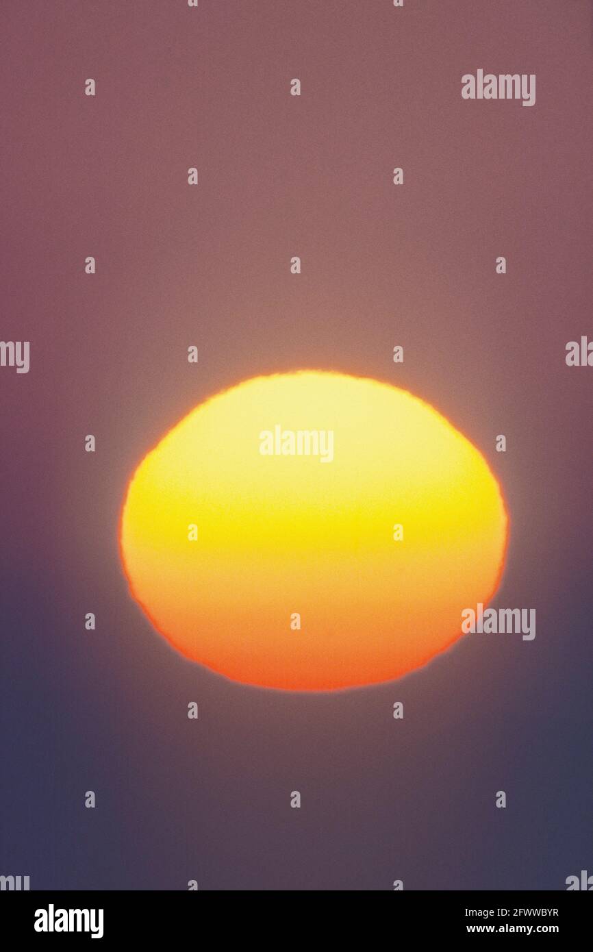 Le soleil bas dans le ciel vu à travers un téléobjectif de 600 mm; tourné rouge par la distorsion atmosphérique et le smog. Banque D'Images