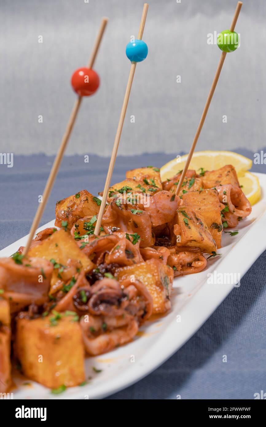 Apéritif ou tapa typiquement espagnol, calmar avec ail et pommes de terre, servi sur un plateau blanc allongé avec fond de citron et rustique. Traditionnel Banque D'Images