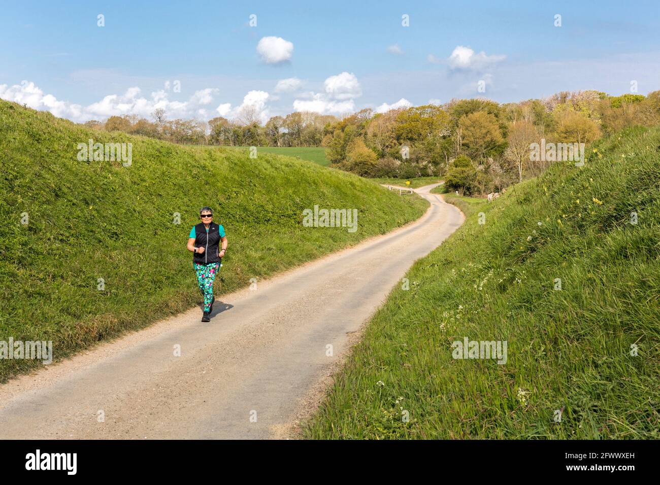 Une femme qui s'exerce, qui court sur une voie de campagne. Suffolk, Royaume-Uni. Banque D'Images