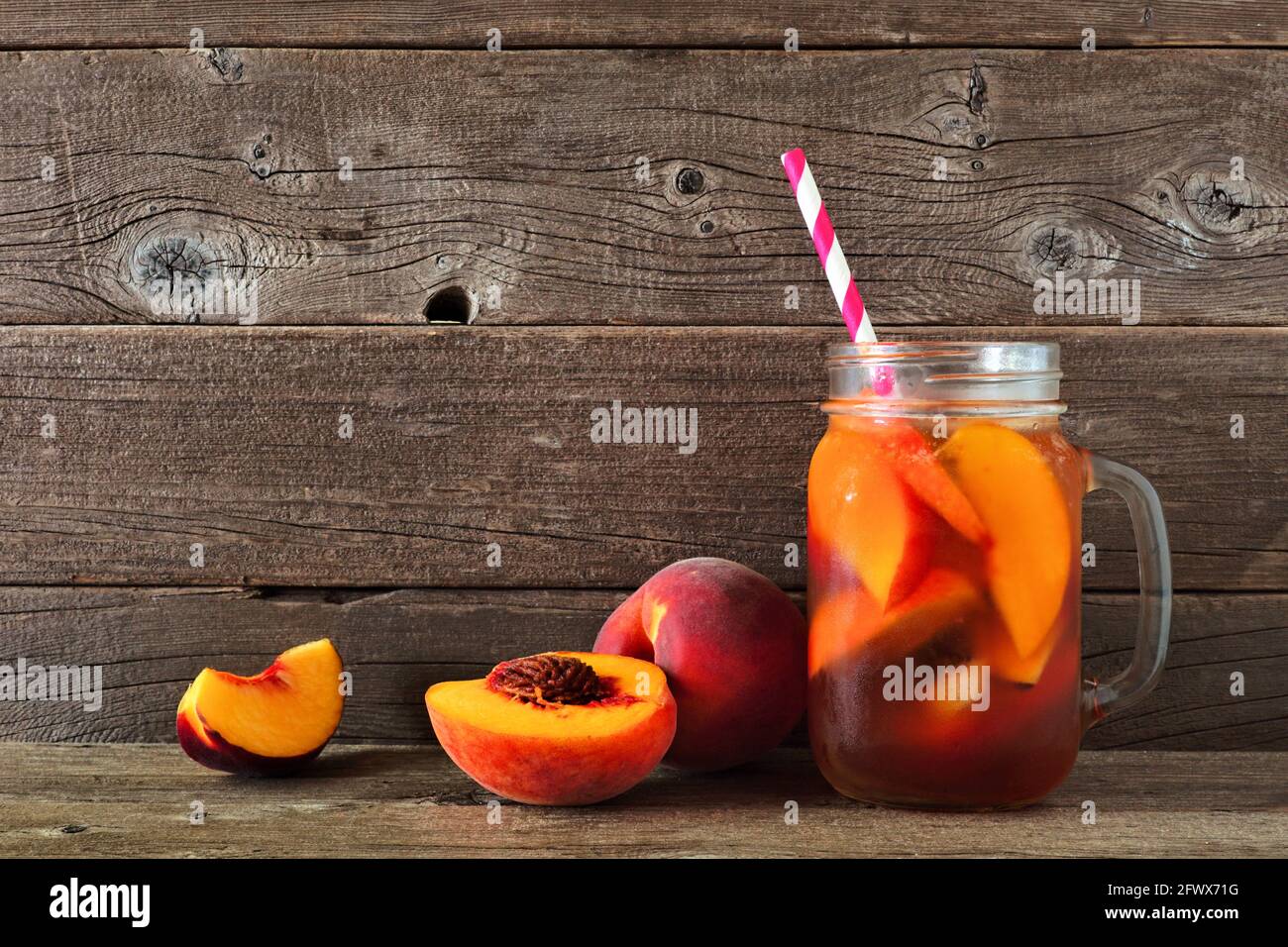 Thé glacé à la pêche fait maison dans un pot en verre maçon. Vue latérale avec fruits coupés sur fond de bois rustique. Banque D'Images