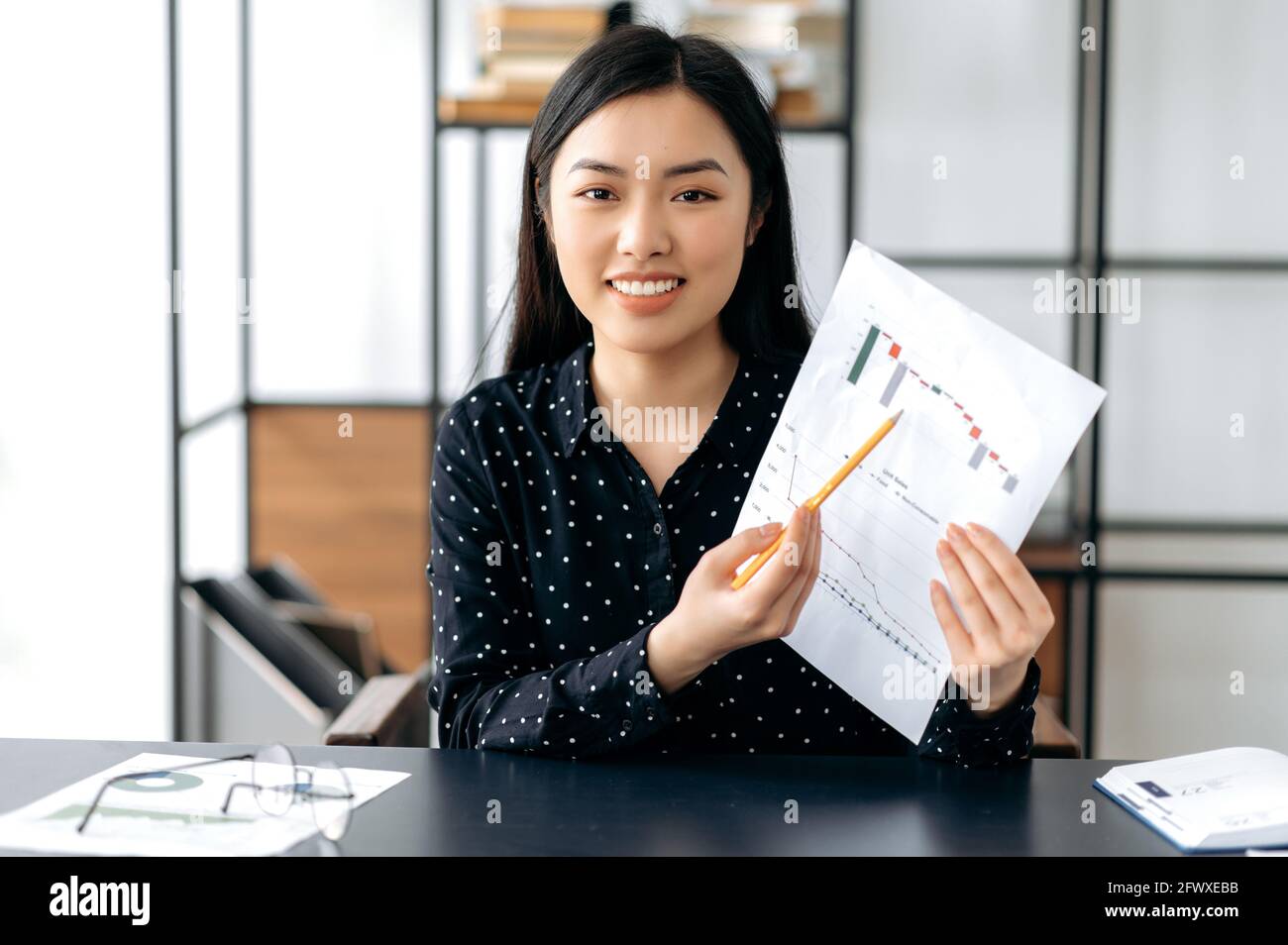 Une femme d'affaires asiatique, un coach financier ou un responsable de haut niveau, qui a réussi à être attirante et confiante, s'entretient avec des collègues ou des clients par liaison vidéo, affiche des graphiques, mène des consultations, sourit Banque D'Images