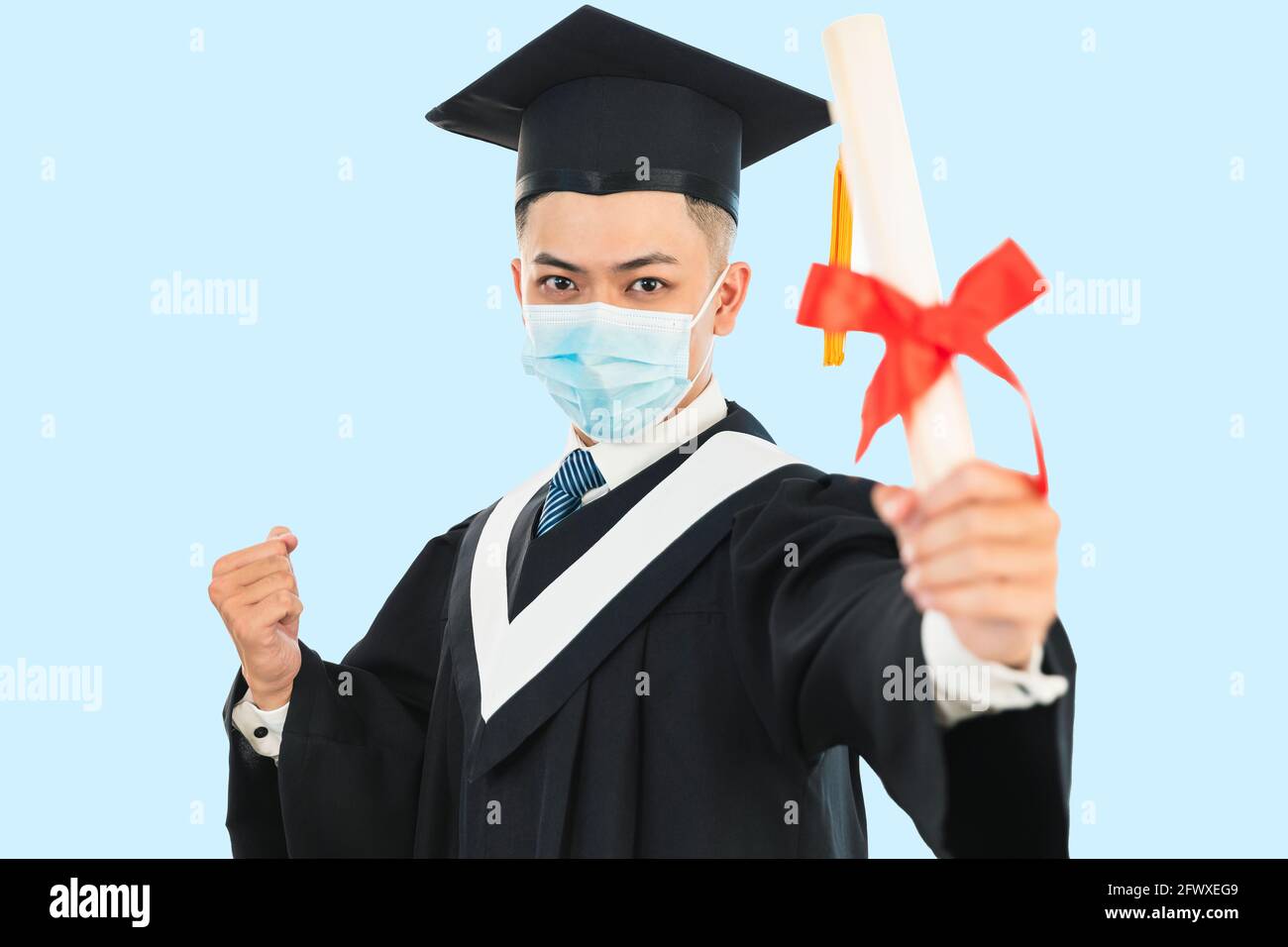 jeune homme graduation portant un masque facial et tenant son collège certificat pendant la pandémie du coronavirus Banque D'Images
