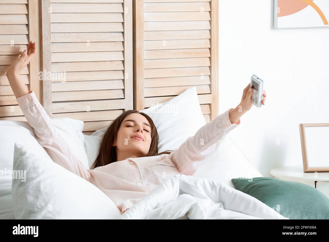 Jeune femme avec la télécommande de climatisation couché dans le lit Photo  Stock - Alamy