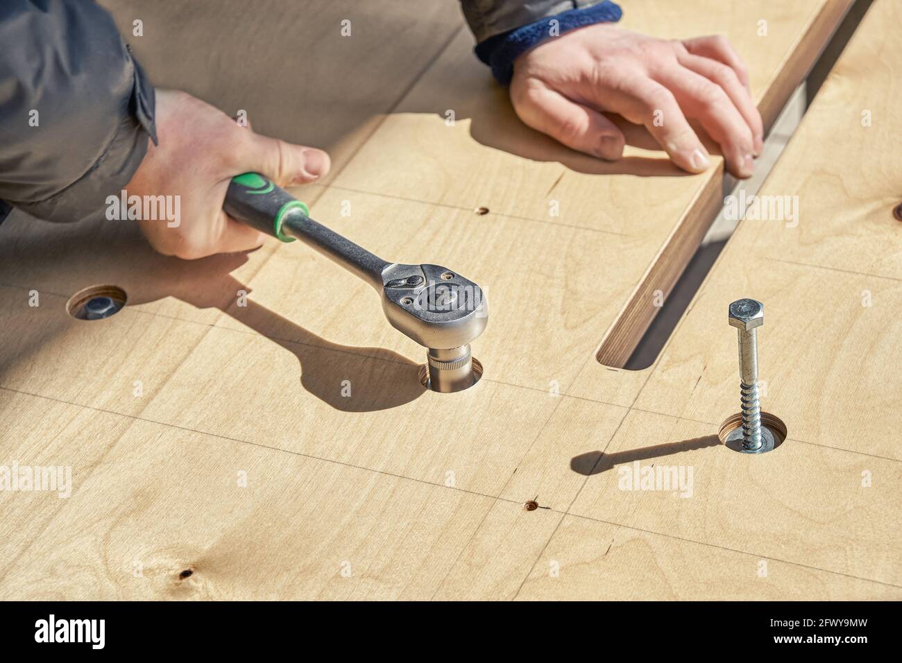 Un artisan qualifié assemble les vis tournantes de la grande table à manger en bois avec clé à l'extérieur, vue de très près par temps ensoleillé Banque D'Images