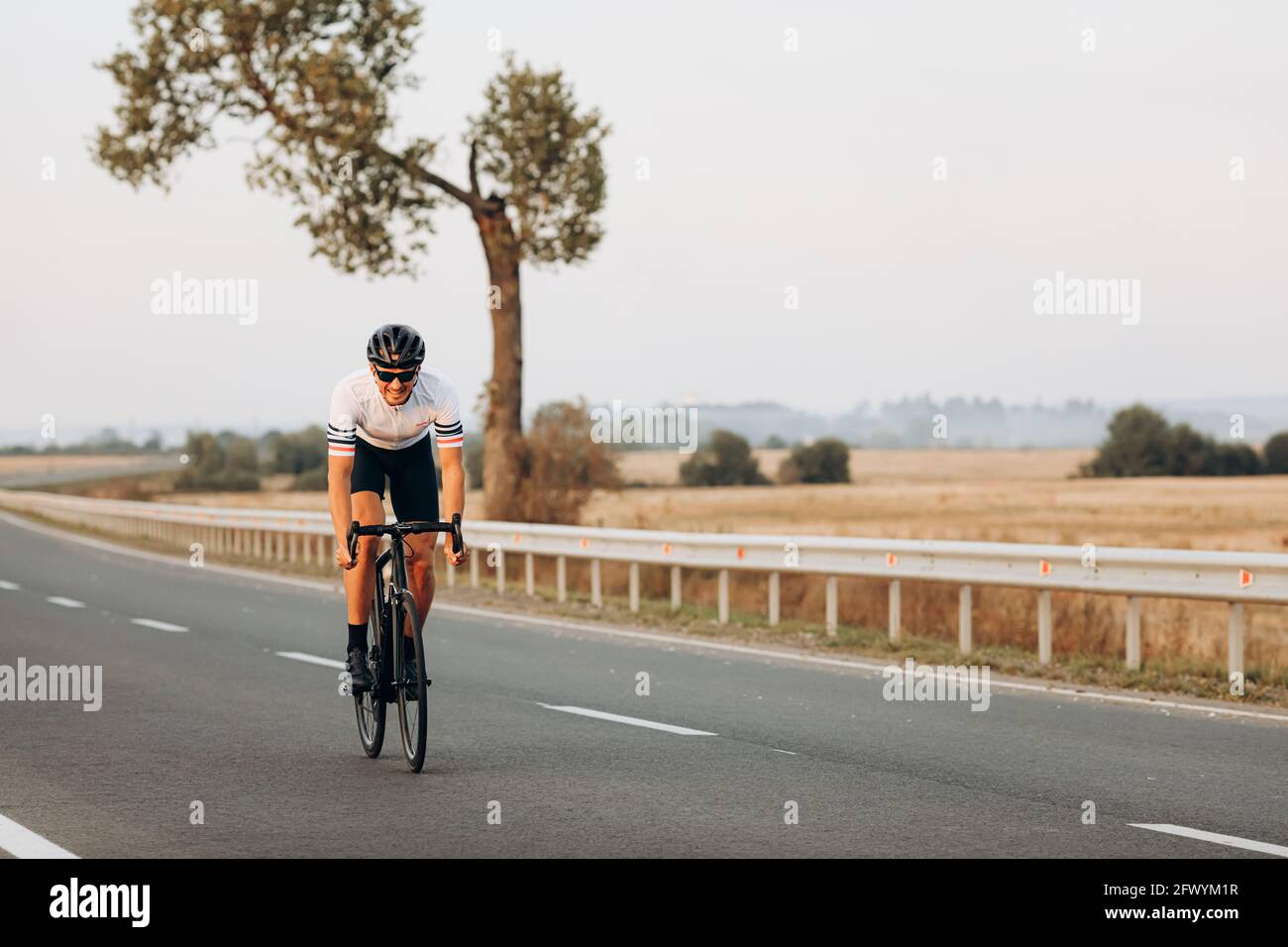 Homme joyeux faisant du vélo sur une route pavée au milieu de la campagne Banque D'Images