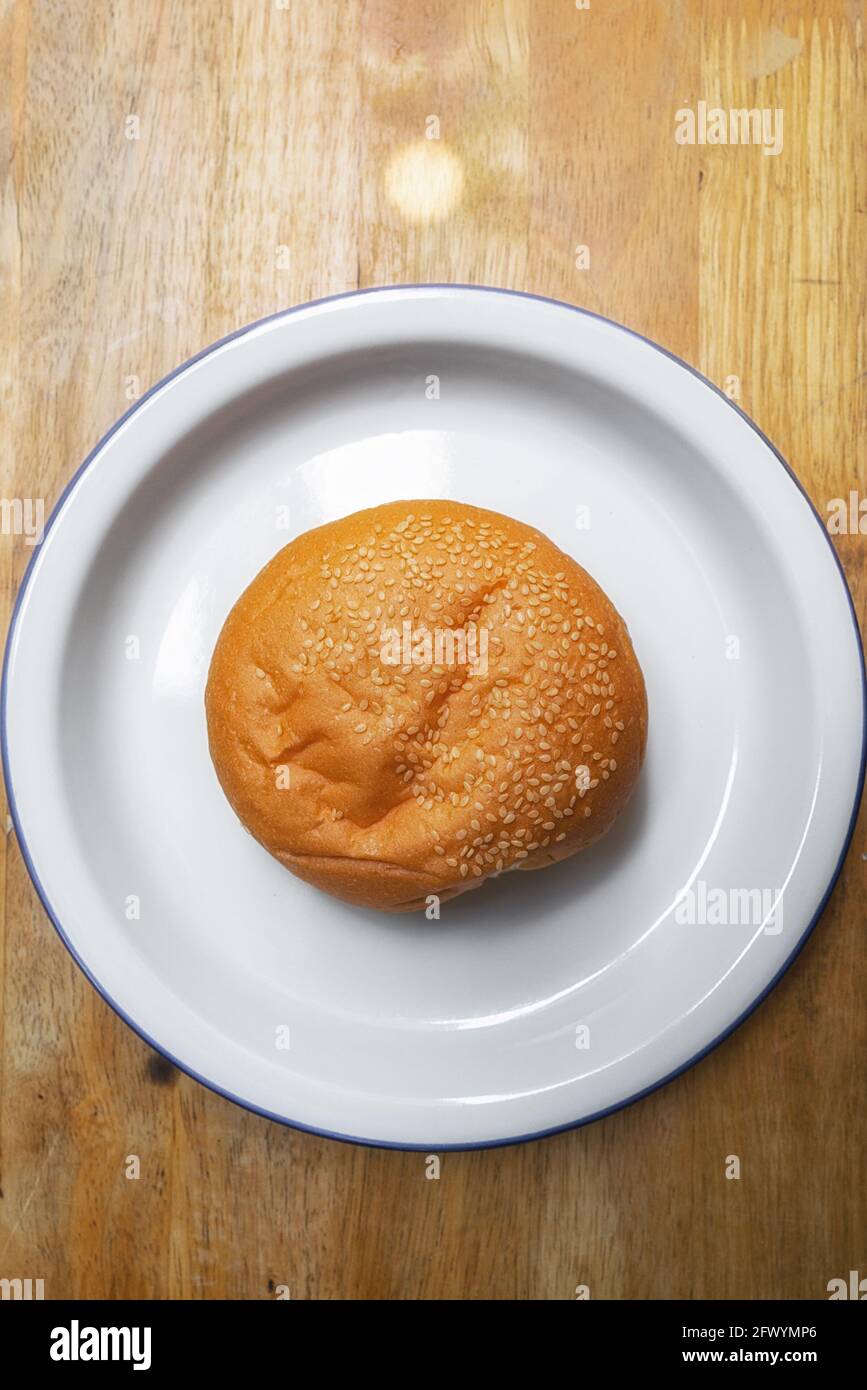 hamburger rond doux aux graines de sésame dorées et fraîches dans un plat blanc sur une table en bois Banque D'Images