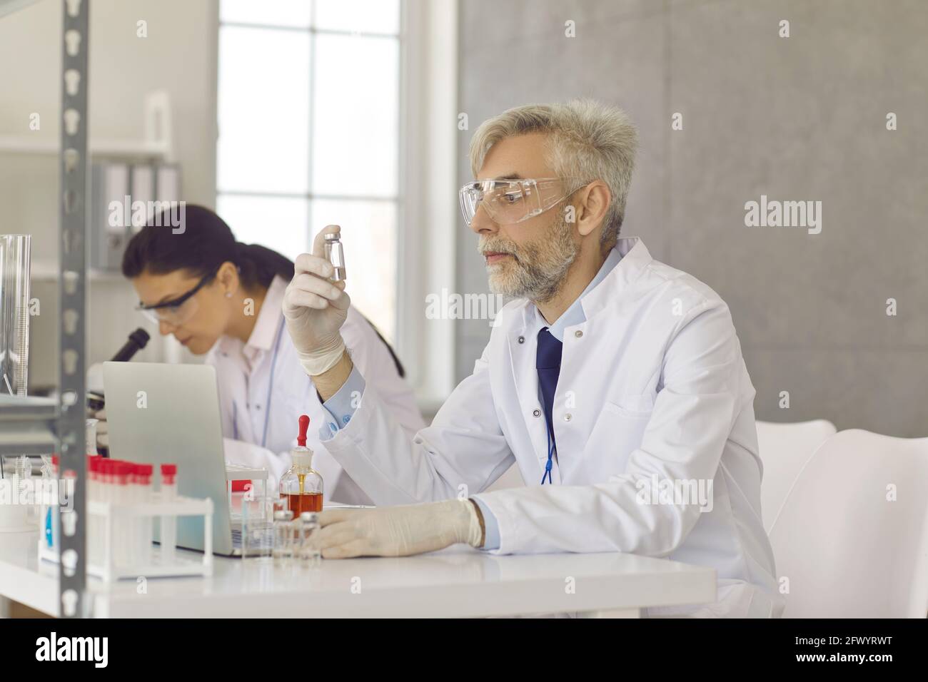 Scientifique sérieux dans des lunettes et des gants travaillant sur un nouveau vaccin en laboratoire Banque D'Images