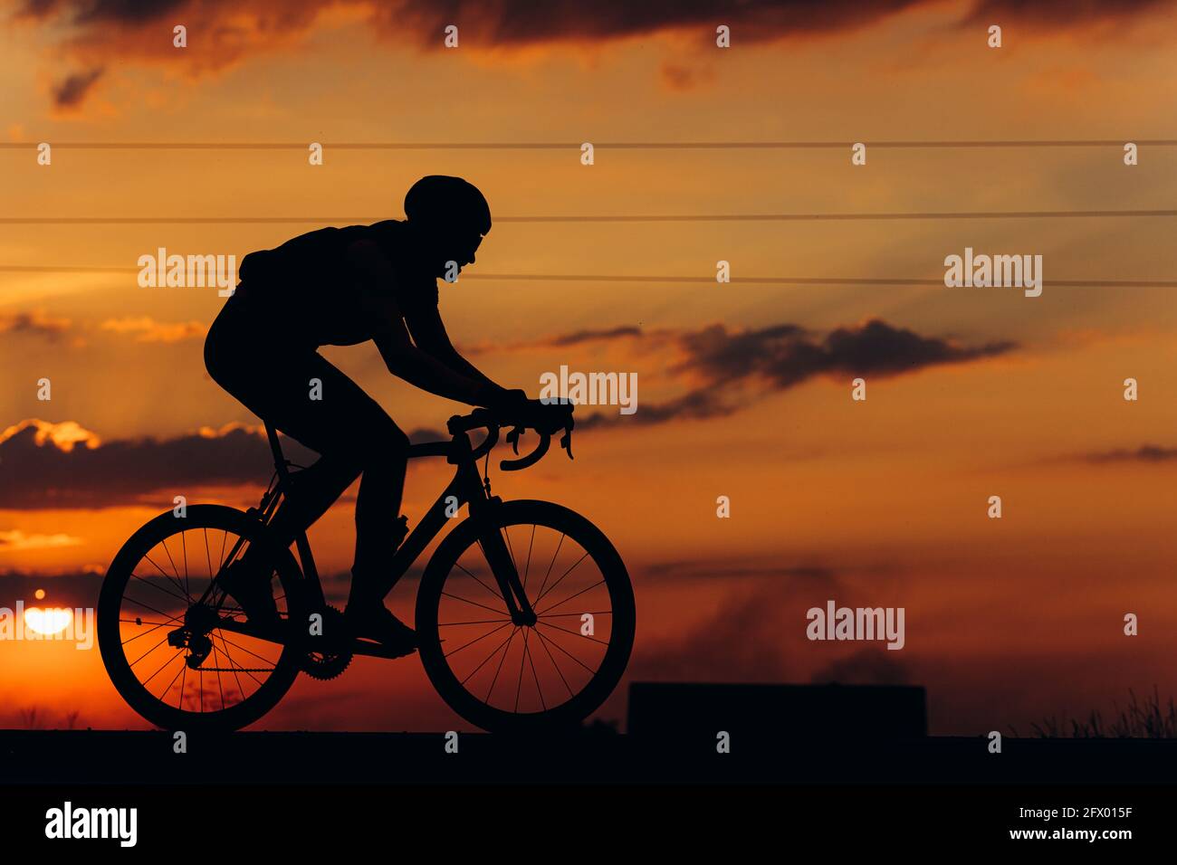 Silhouette d'homme en vélo sur la route pendant le coucher du soleil Banque D'Images