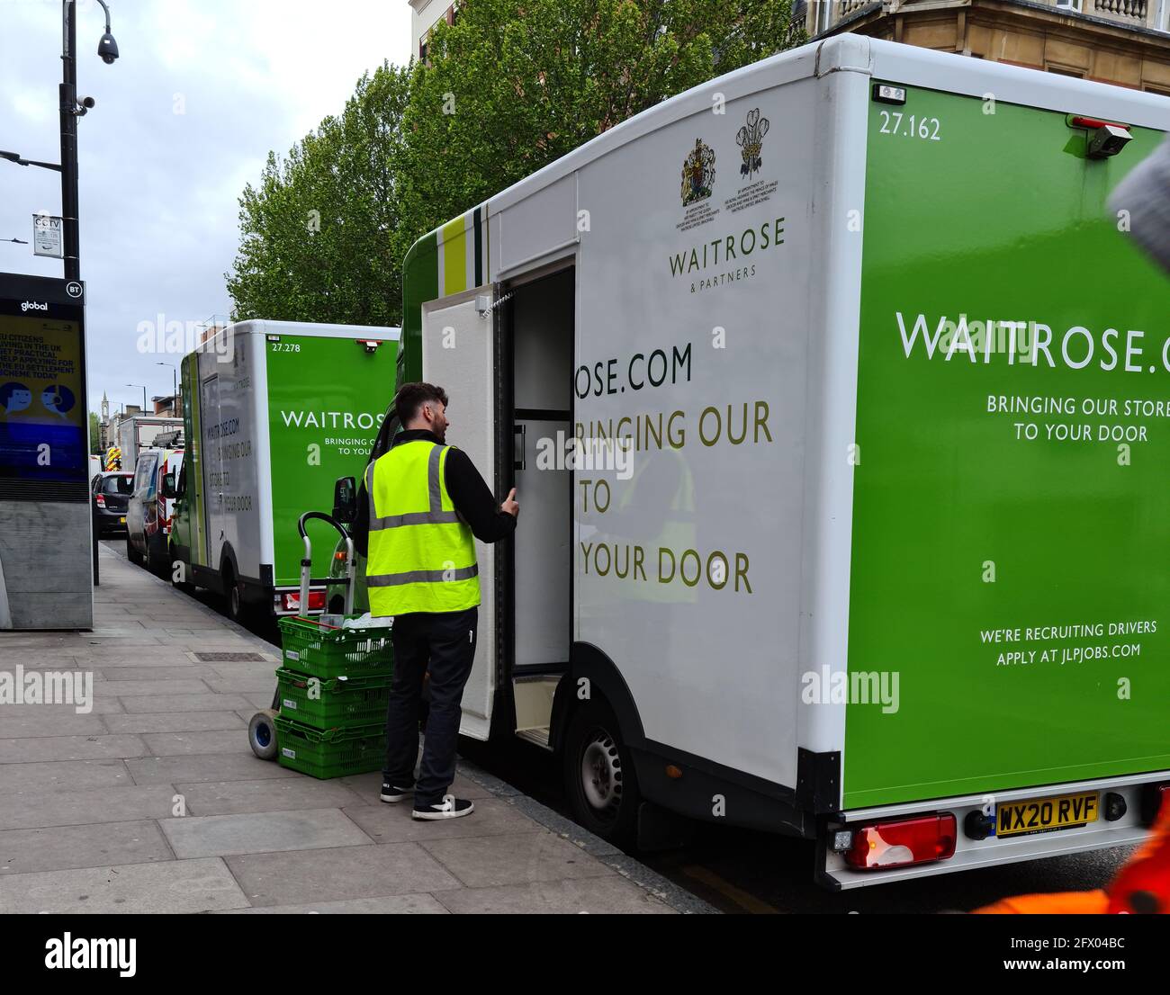 Londres. ROYAUME-UNI- 05.21.2021. Le supermarché Waitrose en ligne de livraison de produits alimentaires sur une rue avec chauffeur déchargement des paniers de provisions. Banque D'Images