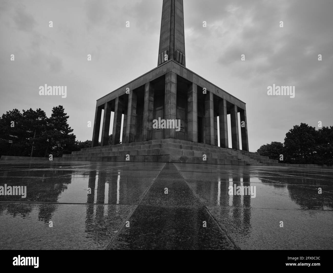 Vue en noir et blanc pluvieuse du mémorial de guerre de Slavin à Bratislava, Slovaquie, avec un pavé mouillé réfléchissant et un ciel dramatique Banque D'Images