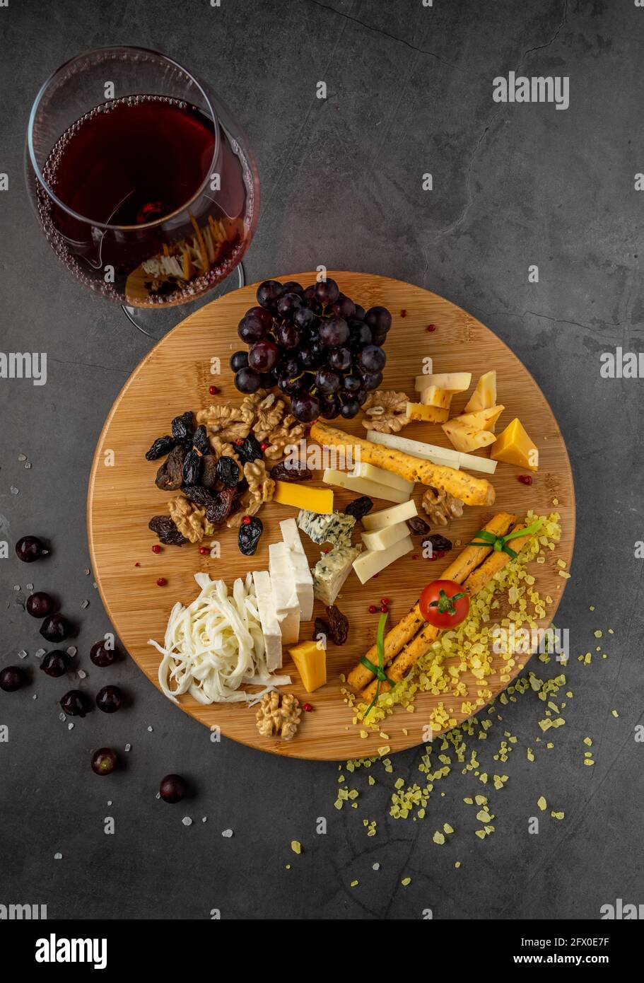 Assiette de fromages servie avec des raisins, de la confiture, des figues, des craquelins et des noix sur fond de pierre sombre Banque D'Images