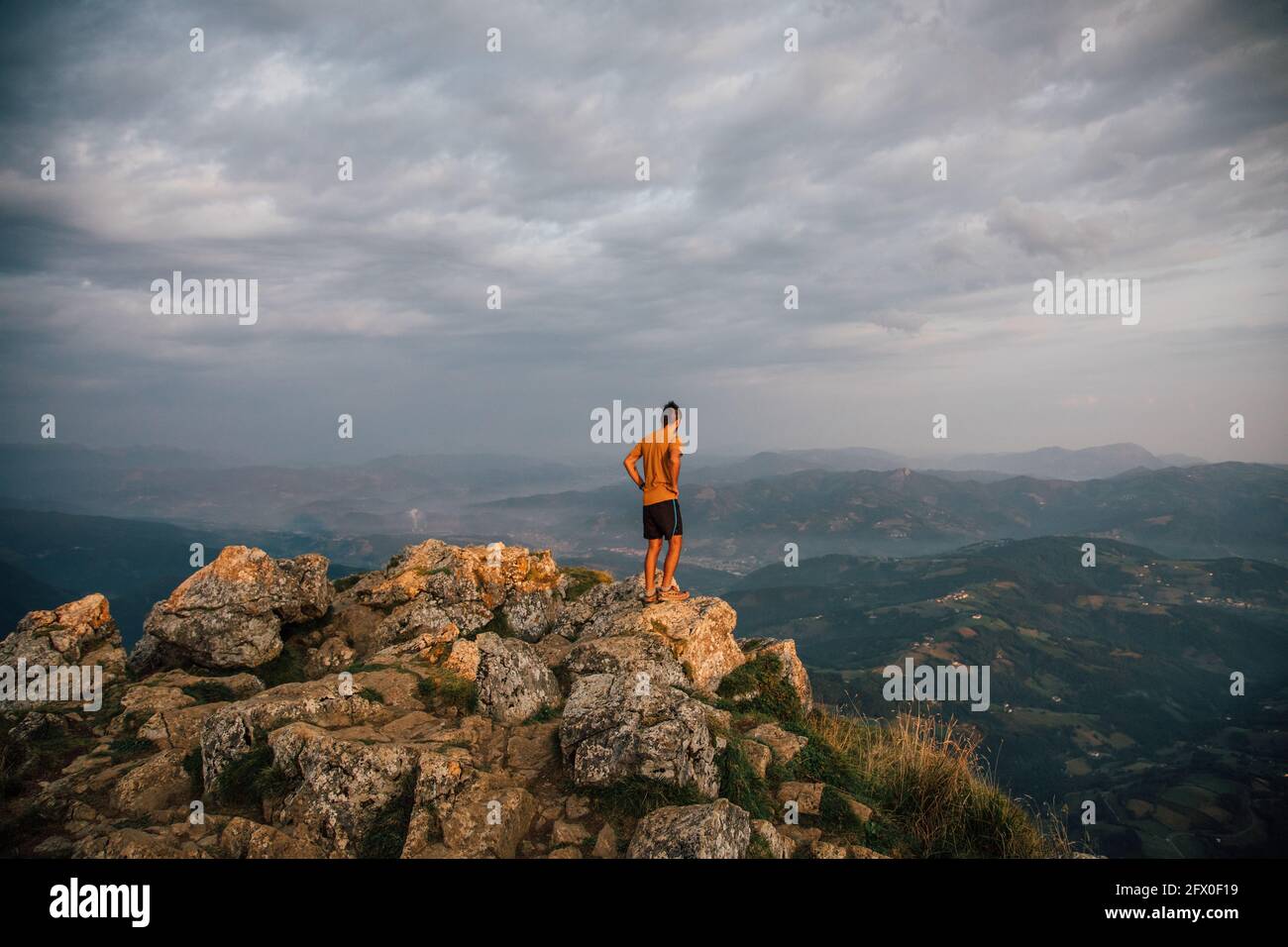 Homme éloigné debout sur le rocher au-dessus de la vallée de highlands sous un ciel sombre dans les nuages Banque D'Images