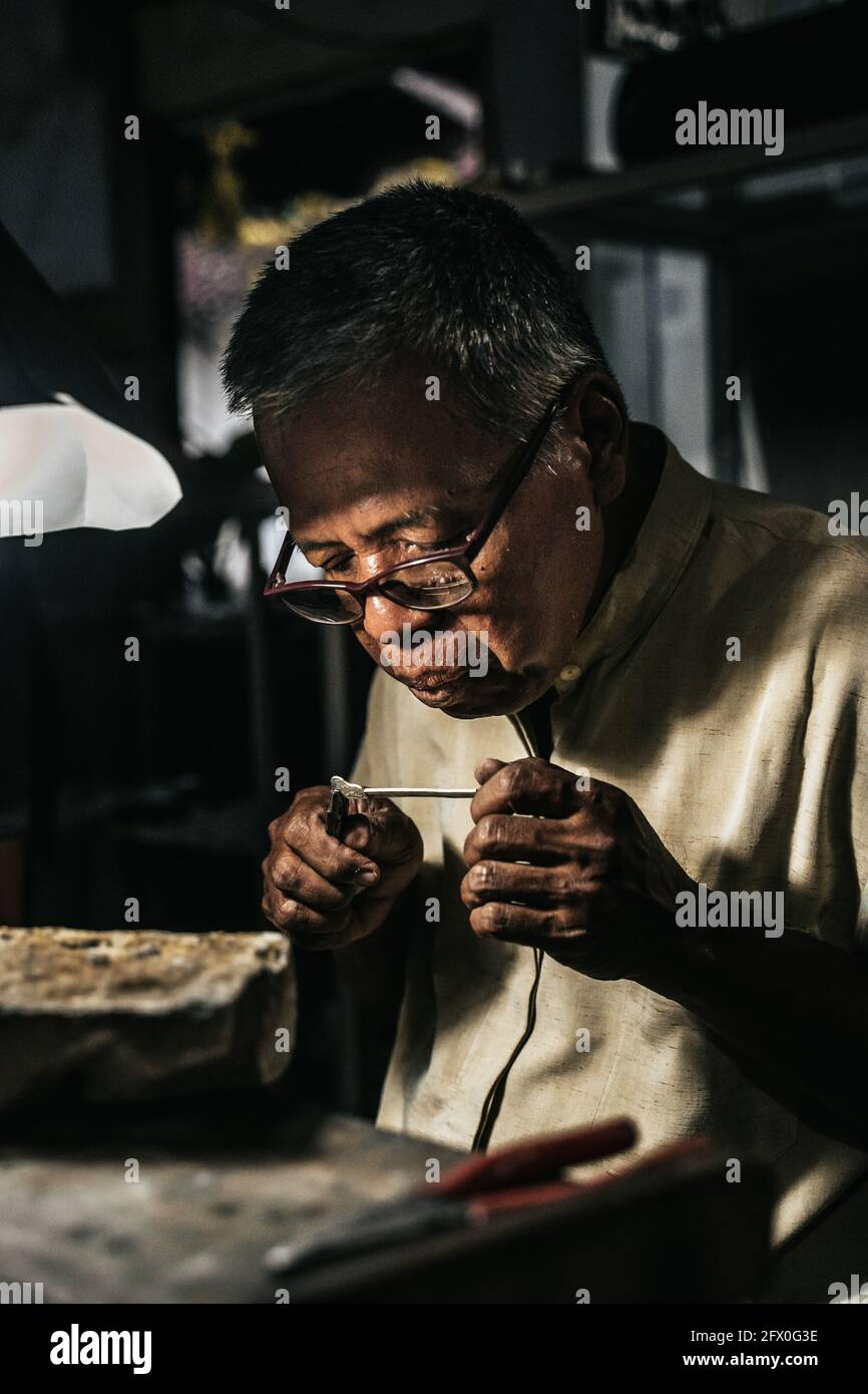 Concentration de l'orfèvre afro-américain senior dans les vêtements décontractés et lunettes tenant la soudure avec des pinces tout en créant des bijoux dans l'atelier Banque D'Images