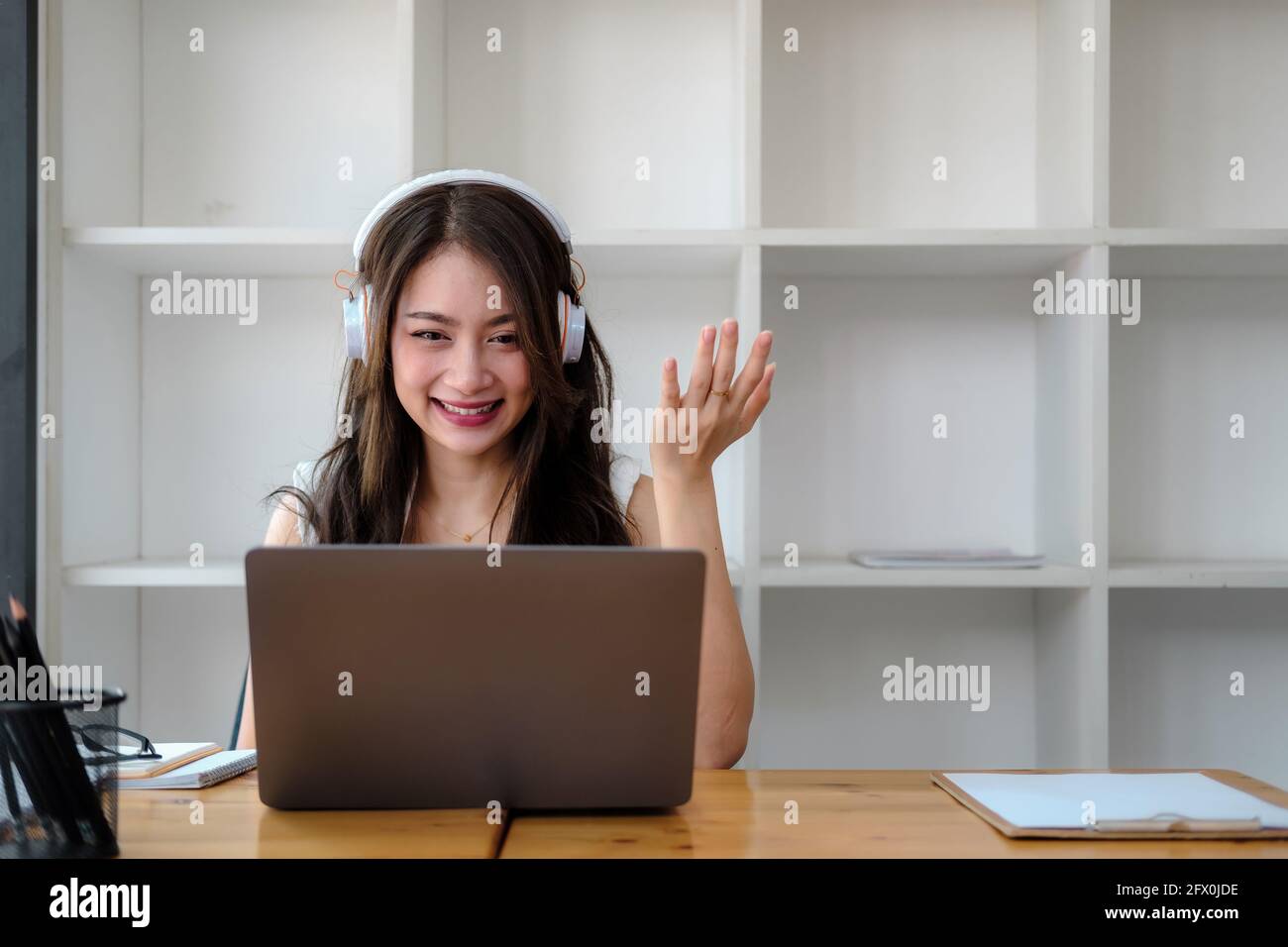 Vue latérale prise de vue en souriant femme asiatique indépendante portant un casque, communiquant avec le client via un appel vidéo sur ordinateur. Professionnel agréable millénaire Banque D'Images