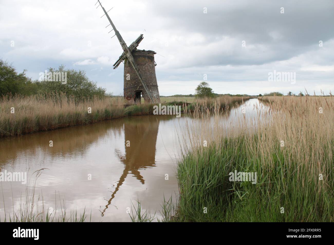 Paysage de l'ancienne pompe de moulin à vent de brique avec des voiles de bois se reflètent dans l'eau de rivière de Norfolk Broads Horsey East Anglia Angleterre par la banque de roseaux herbeux Banque D'Images