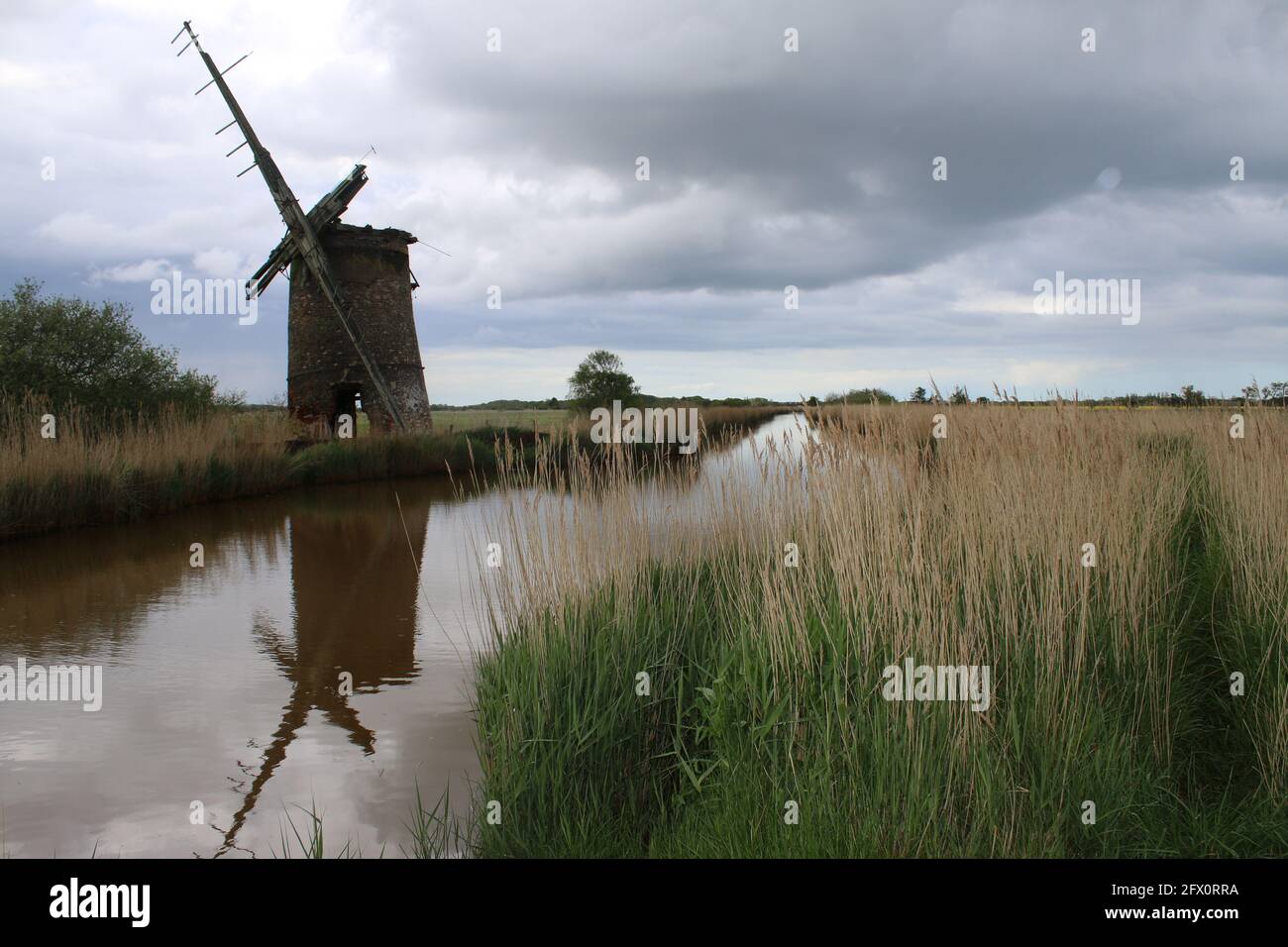 Paysage de l'ancienne pompe de moulin à vent de brique avec des voiles de bois se reflètent dans l'eau de rivière de Norfolk Broads Horsey East Anglia Angleterre par la banque de roseaux herbeux Banque D'Images