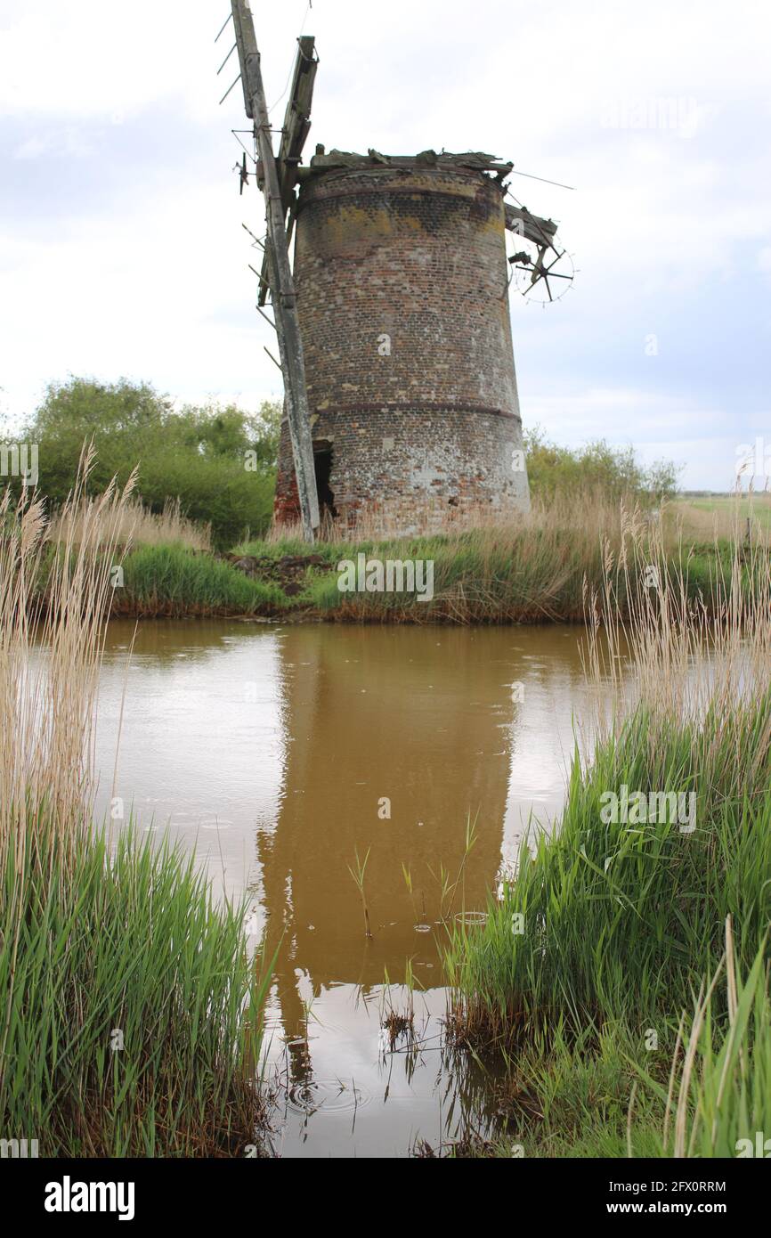 Paysage de l'ancienne pompe de moulin à vent de brique avec des voiles de bois se reflètent dans l'eau de rivière de Norfolk Broads Horsey East Anglia Angleterre par la banque de roseaux herbeux Banque D'Images