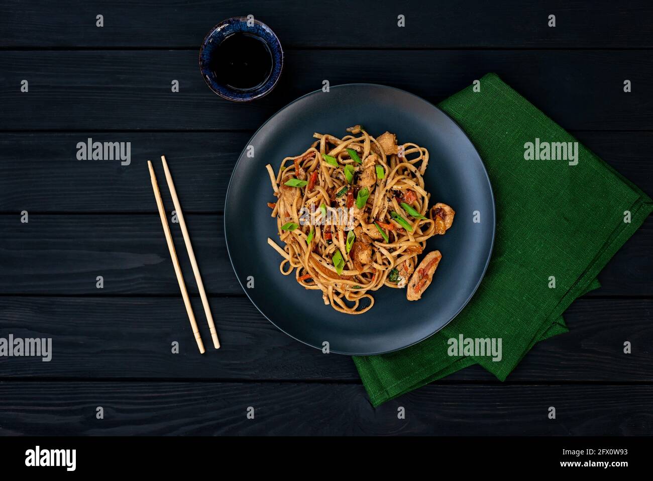 Nouilles udon asiatiques avec légumes de poulet et sauce teriyaki sur fond de bois noir. Cuisine chinoise et japonaise. Banque D'Images