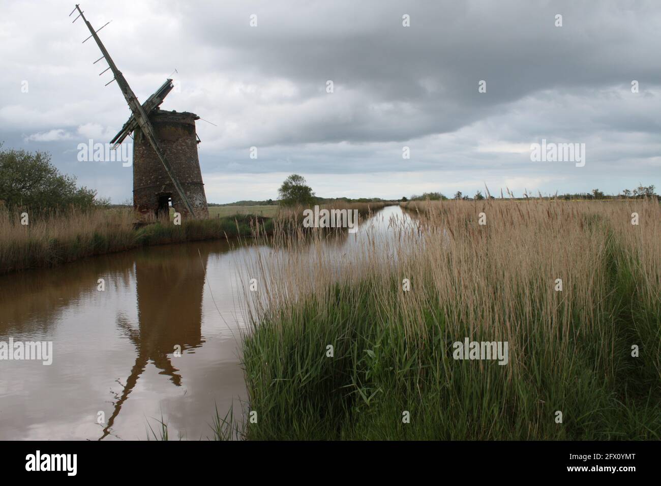 Paysage de l'ancien moulin à vent de brique pompe des voiles de bois se reflètent Dans l'eau de la rivière de Norfolk Broads à Horsey East Anglia Angleterre royaume-uni sur la banque de roseau Spring Banque D'Images