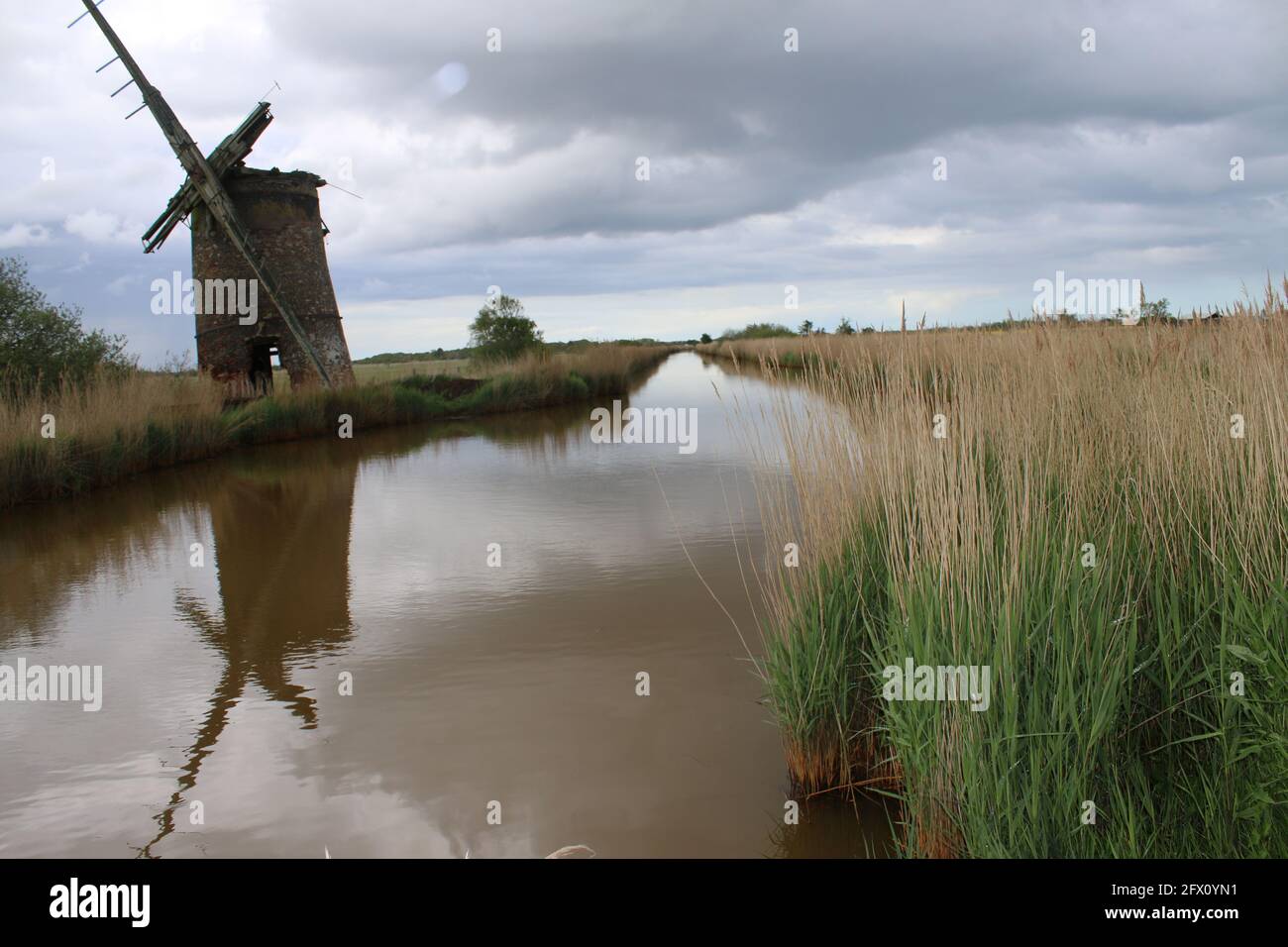 Paysage de l'ancien moulin à vent de brique pompe des voiles de bois se reflètent Dans l'eau de la rivière de Norfolk Broads à Horsey East Anglia Angleterre royaume-uni sur la banque de roseau Spring Banque D'Images