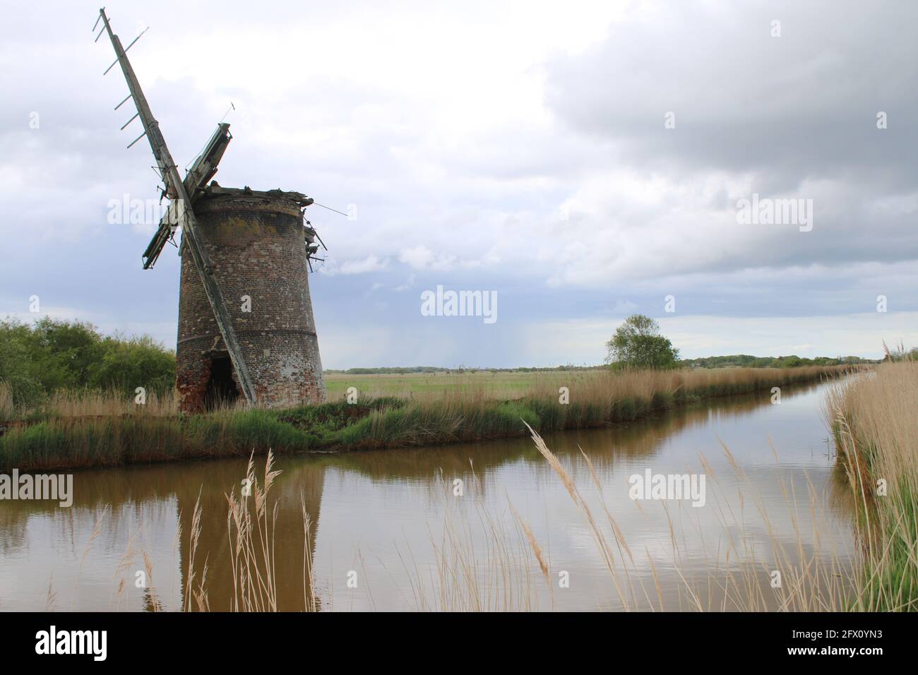 Paysage de l'ancien moulin à vent de brique pompe des voiles de bois se reflètent Dans l'eau de la rivière de Norfolk Broads à Horsey East Anglia Angleterre royaume-uni sur la banque de roseau Spring Banque D'Images