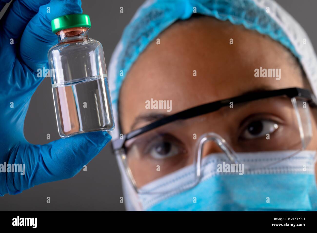 Gros plan de la femme chirurgien tenant la bouteille de vaccin Covid-19 contre arrière-plan gris Banque D'Images