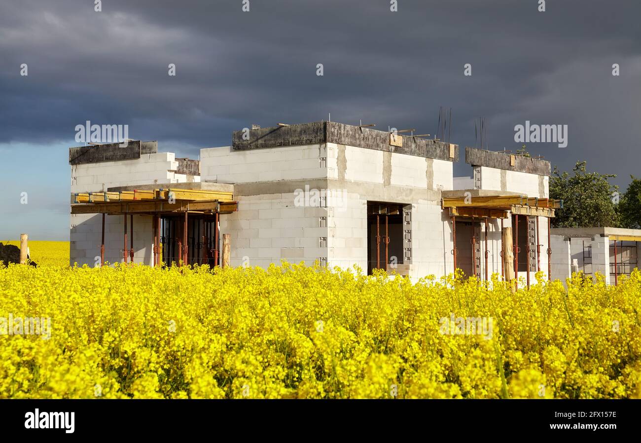 Maison familiale rurale en construction avec champ de colza en premier plan et nuages orageux en arrière-plan. Banque D'Images