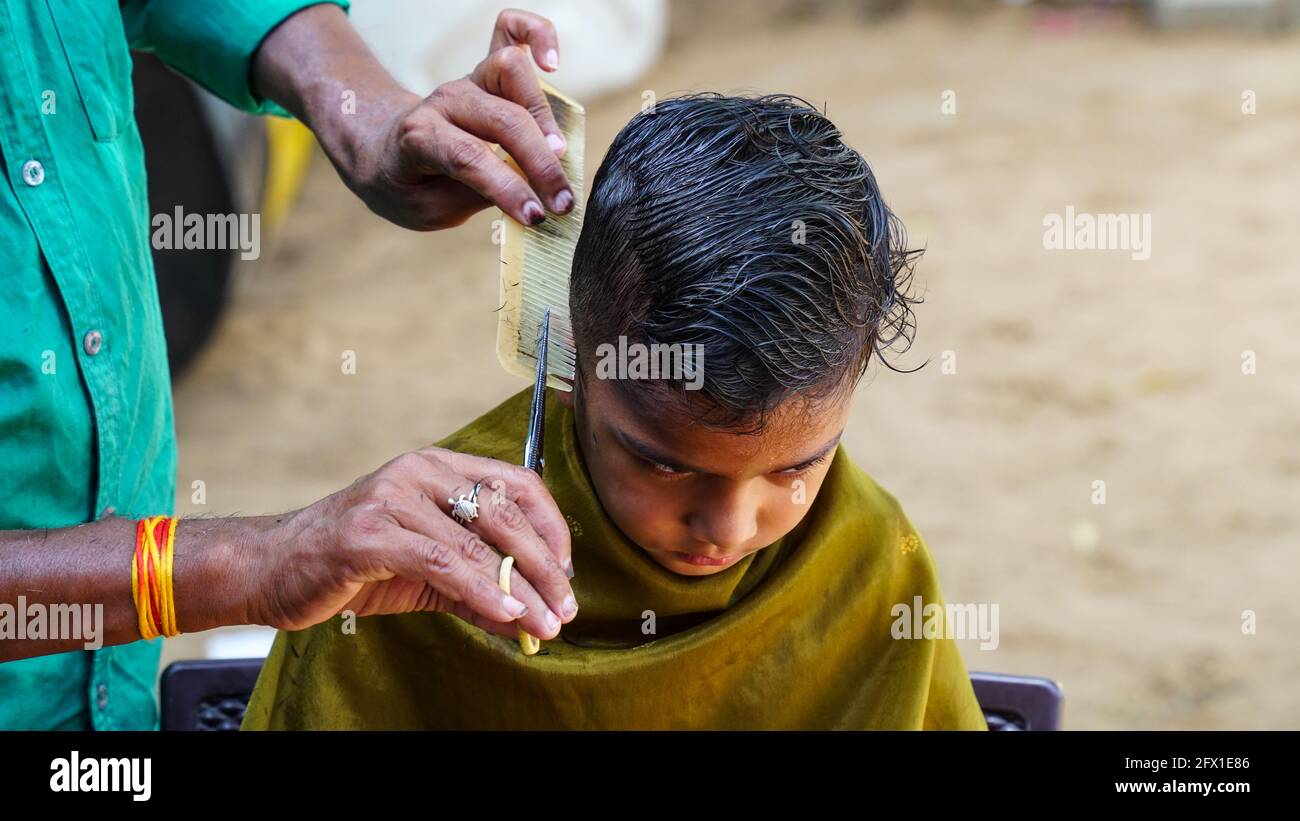 Indian barber travaillant dans les rues du village en une journée ensoleillée. Un barbier coupant les cheveux d'un garçon indien pendant le confinement en Inde. Banque D'Images