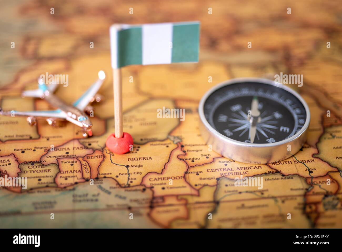 Le drapeau du Nigeria, un avion et une boussole sur la carte du monde. Le concept de voyage et de tourisme. Banque D'Images