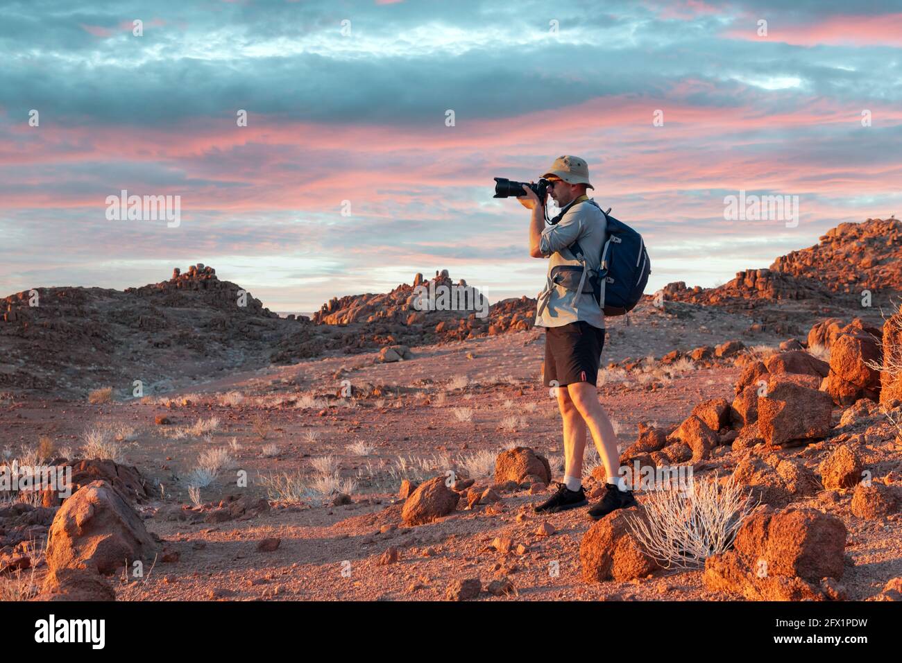 Photographe prenant des photos dans les rochers du désert de Namib, Namibie, Afrique. Montagnes rouges et ciel de coucher de soleil en arrière-plan. Photographie de paysage Banque D'Images