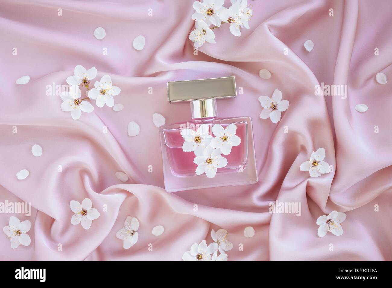 Bouteille en verre de parfum de luxe aromatique sur un tissu en soie rose doux avec fleurs de la branche. Emballage minimaliste, marquage. Floral Banque D'Images