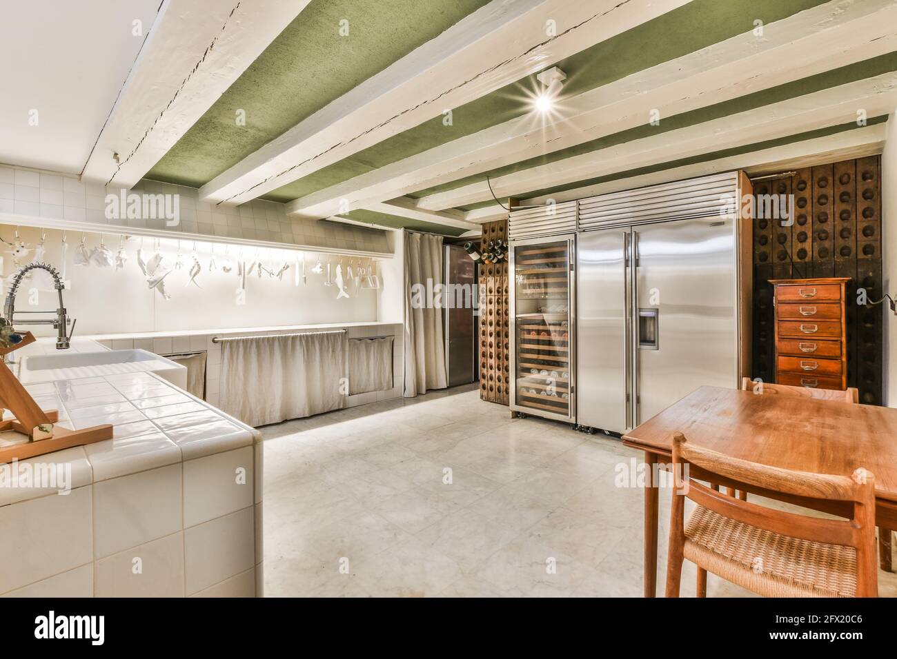Grande cuisine contemporaine de maison de maître avec réfrigérateur en acier inoxydable et casiers à vin en bois sous poutres blanches au plafond Banque D'Images