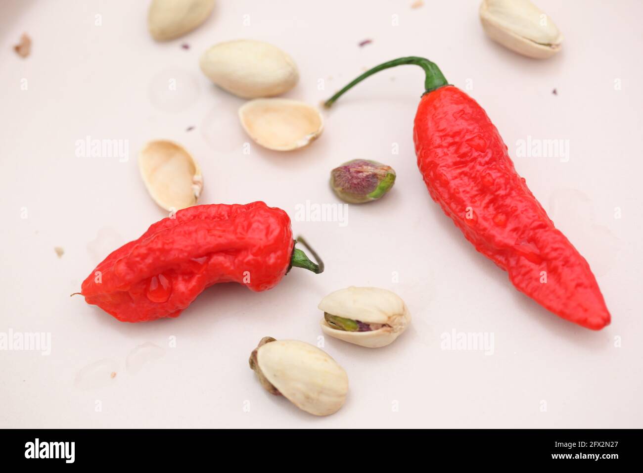Vue sur les Chiles rouges et les pistaches sur la crème céramique rose clair Banque D'Images