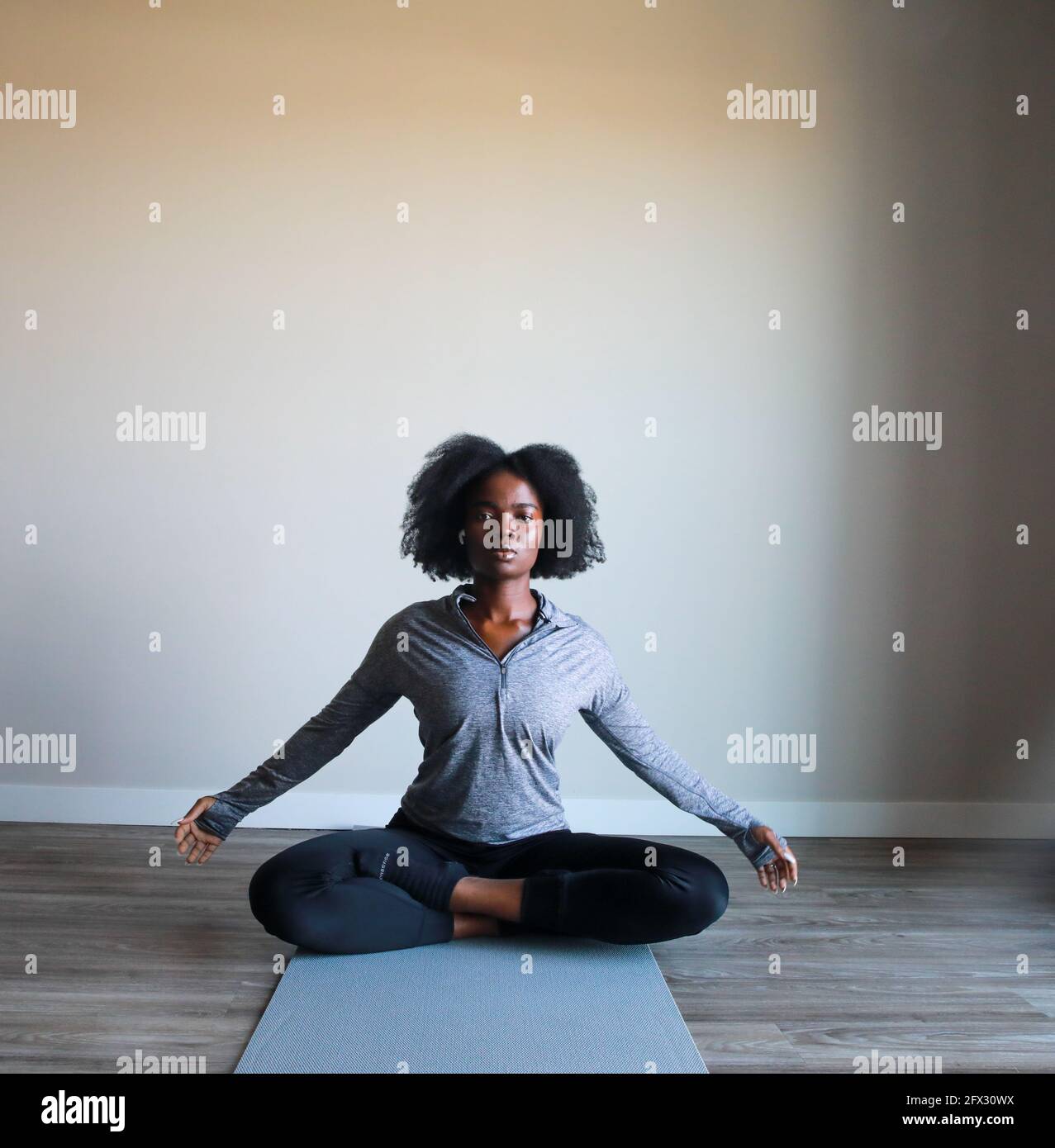 Belle jeune femme noire assise en position de yoga et méditant isolée sur fond blanc. Banque D'Images