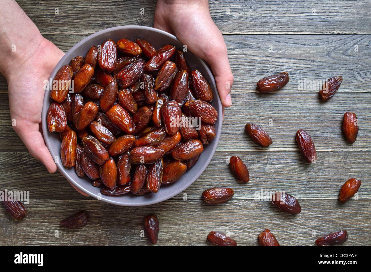 Les mains tiennent les fruits secs dattes dans un bol en céramique sur un fond en bois. Fruits secs biologiques. Vue de dessus. Pose à plat Banque D'Images