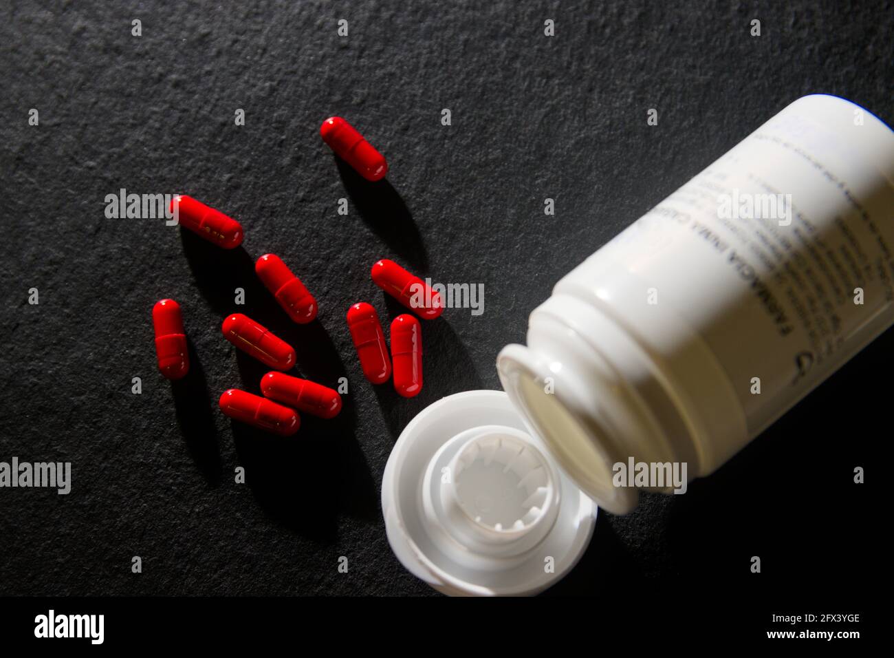 Gros plan de quelques capsules rouges prescrites par un médecin sur un arrière-plan noir à côté du conteneur où ils se trouvent enregistré Banque D'Images