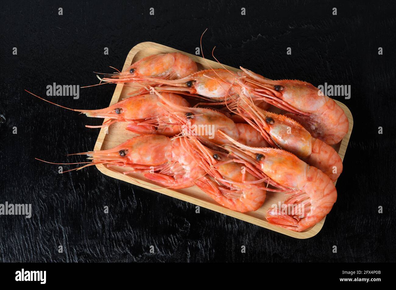 Crevettes cuites dans une coquille sur une plaque de bambou en bois sur une surface en bois noir. Mise au point sélective. Banque D'Images