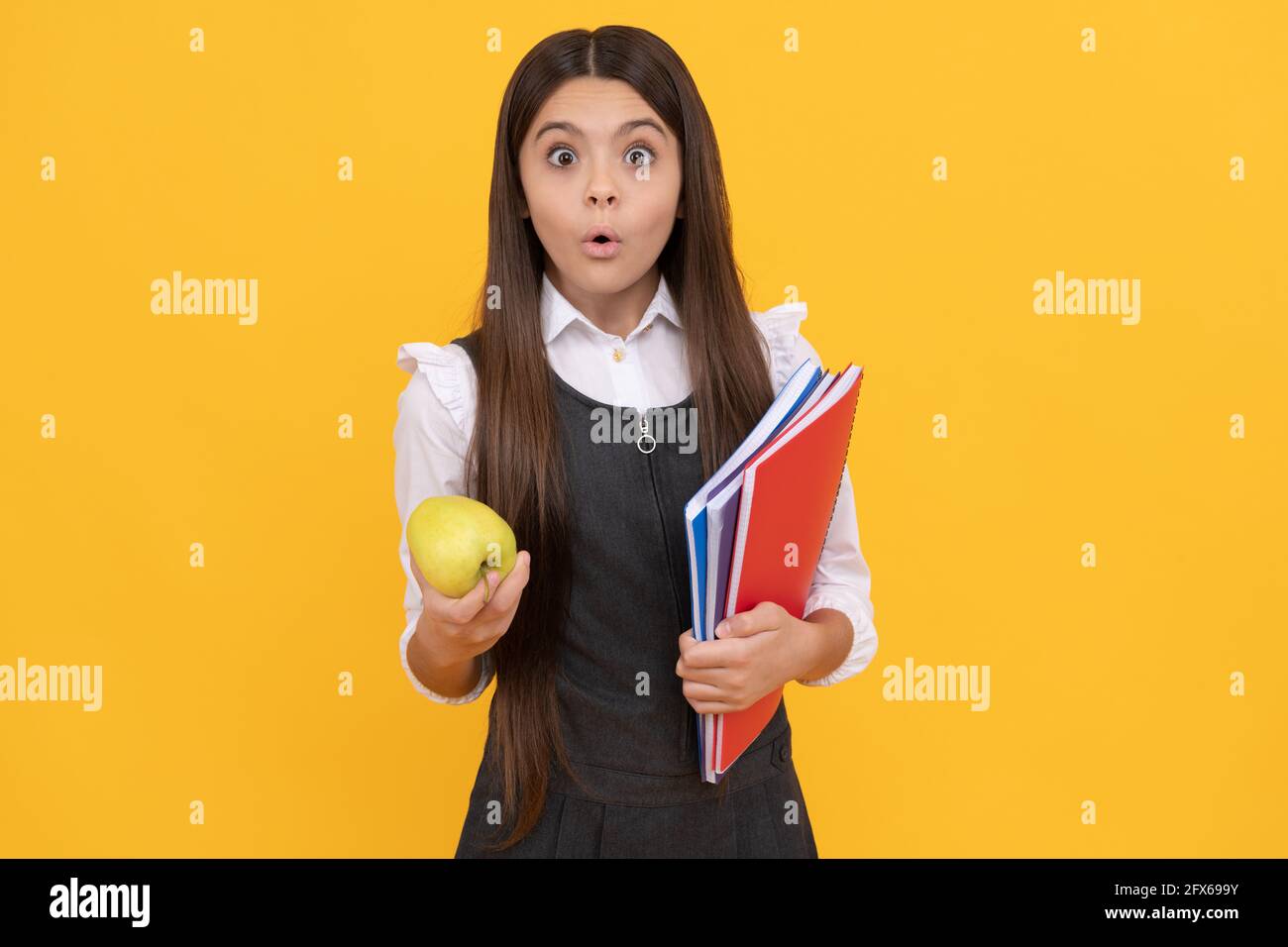 Fille surprise garde d'enfant pomme et école manuels fond jaune, devoirs Banque D'Images